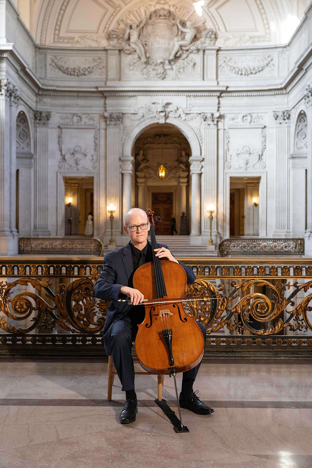 Ben Welch Snellings in formal attire poses with a cello against a grand, ornate architectural backdrop, highlighting the intersection of music and culture.