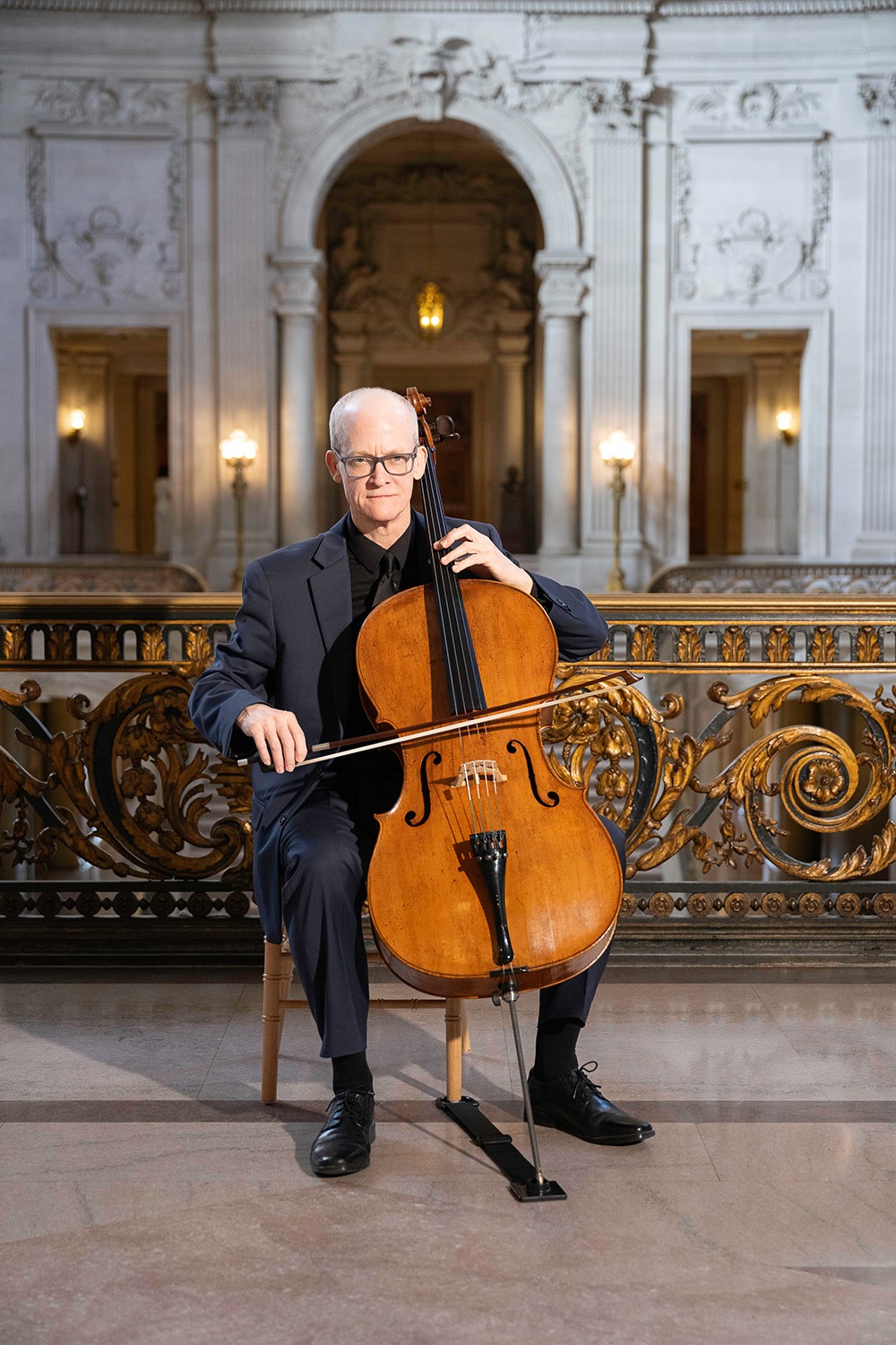 Ben Welch Snellings in formal attire plays a cello in an elegant, historic setting, emphasizing the cultural and musical ambiance of the location.