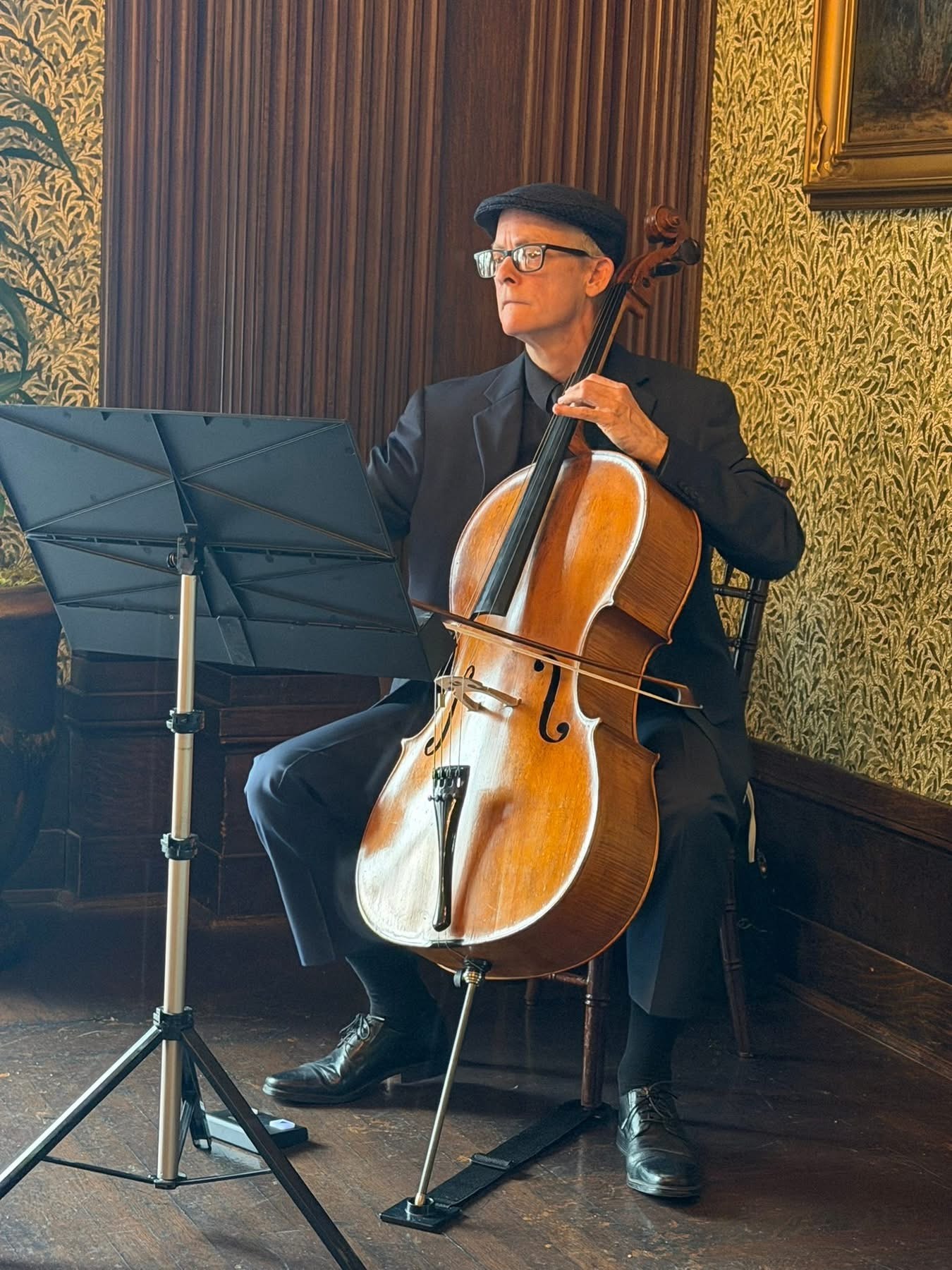 Ben Welch Snellings in formal attire plays seated, focused on his music, with a vintage interior backdrop featuring ornate wallpaper and decorative details.