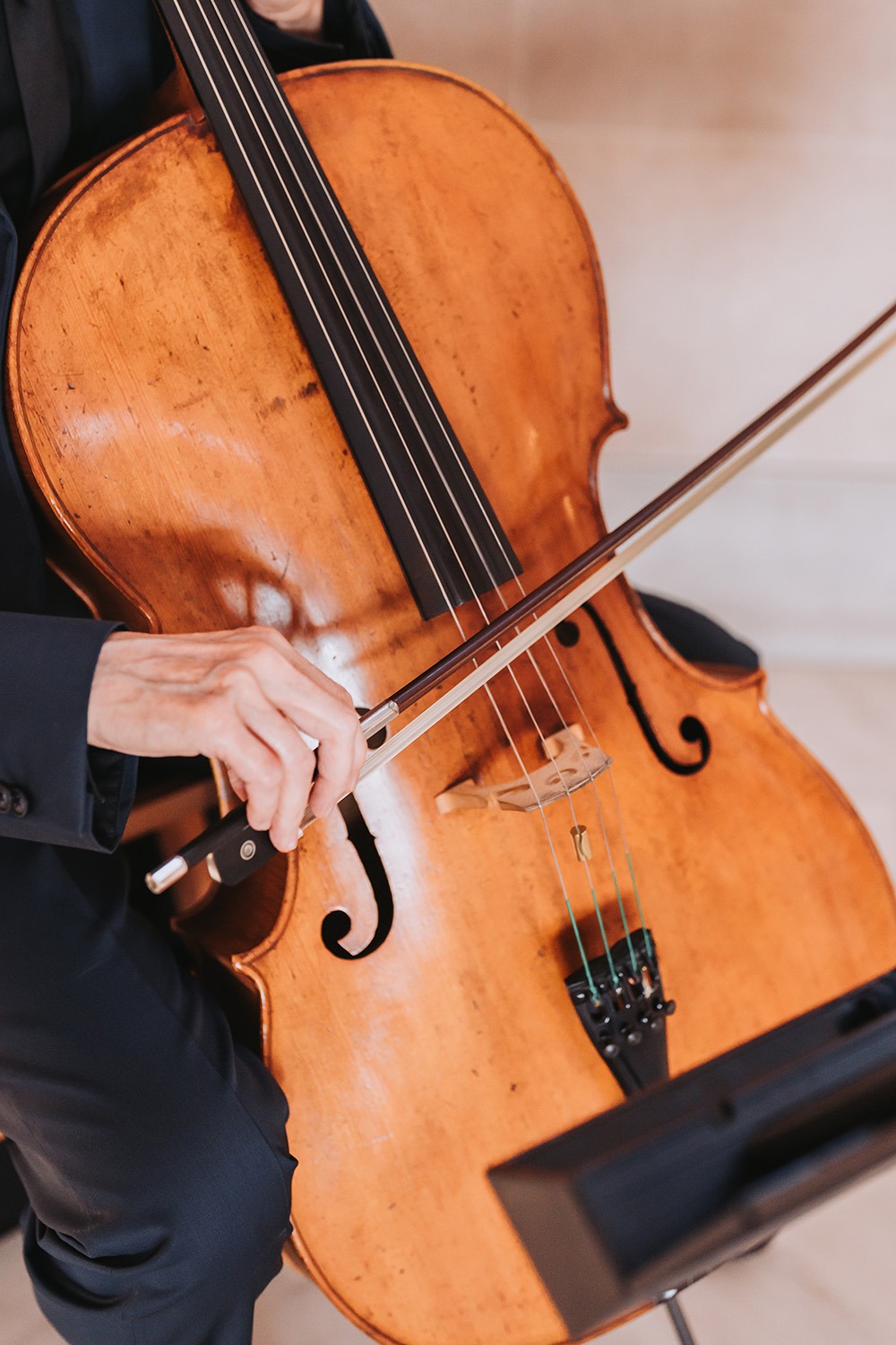 Cellist plays a wooden cello with a bow in their right hand, showcasing the instrument’s craftsmanship and the act of making music.